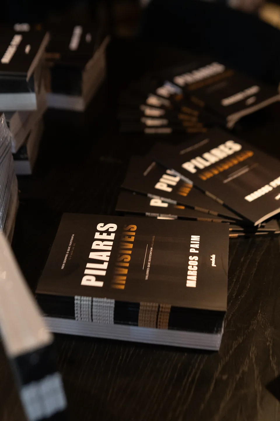 Livro Pilares Invisíveis em destaque, com outros exemplares ao fundo